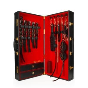 Coffret BDSM ouvert en cuir noir avec intérieur rouge, présentant un ensemble d’accessoires assortis comprenant menottes, sangles, cravaches et chaînes, disposés de manière ordonnée dans une esthétique luxueuse.