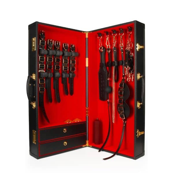 Caja BDSM abierta de cuero negro con interior rojo, que incluye un conjunto de accesorios variados como esposas, correas, fustas y cadenas, ordenados en una estética de lujo.
