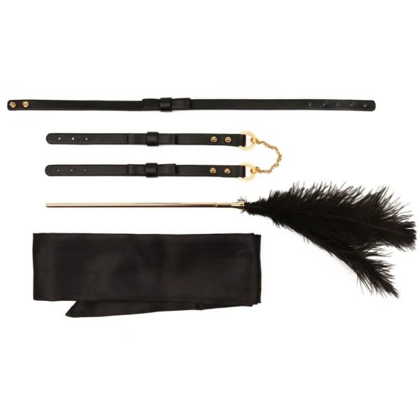 Set BDSM en cuir noir composé de liens ajustables avec anneaux dorés, d’un bandeau en tissu satiné et d’une plume noire montée sur manche doré, présenté sur fond blanc dans une esthétique épurée.