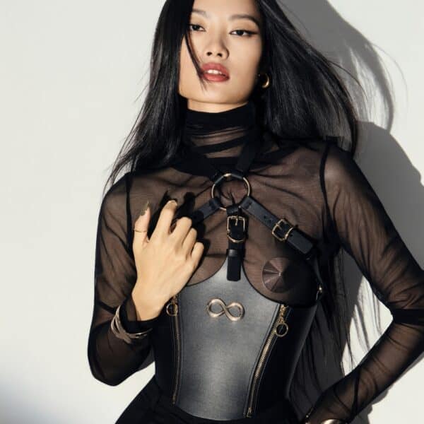 Corset Bondage HOSTIA IINFYNII – Brigade Mondaine Paris Corset Bondage HOSTIA IINFYNII noir avec sangles et anneaux métalliques porté sur un top en mesh, pièce structurée proposée par Brigade Mondaine Paris
