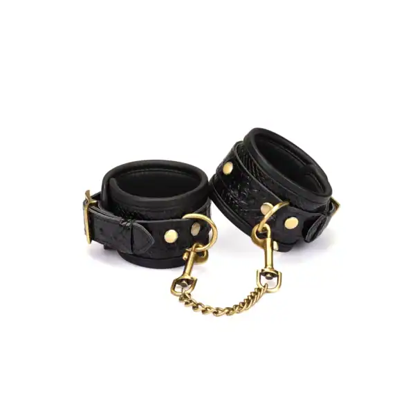 Handschellen aus schwarzem, krokogeprägtem Leder LIEBE SEELE mit Innenfutter und goldener Kette, auf weißem Hintergrund