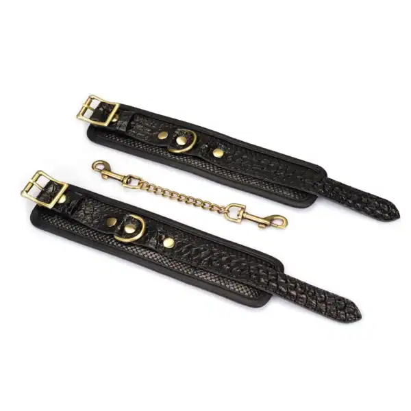 Handschellen aus schwarzem, krokogeprägtem Leder LIEBE SEELE mit Innenfutter und goldener Kette, auf weißem Hintergrund