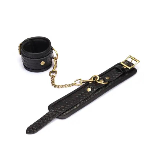 Handschellen aus schwarzem, krokogeprägtem Leder LIEBE SEELE mit Innenfutter und goldener Kette, auf weißem Hintergrund