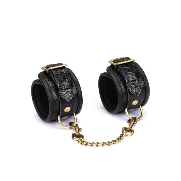 Handschellen aus schwarzem, krokogeprägtem Leder LIEBE SEELE mit Innenfutter und goldener Kette, auf weißem Hintergrund