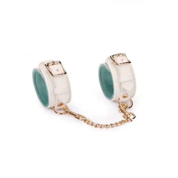 Boudoir Amor handcuffs by Liebe Seele, in light-colored leather with gold chain and snap hooks, presented flat on a light-colored background in the Brigade Mondaine Paris universe.