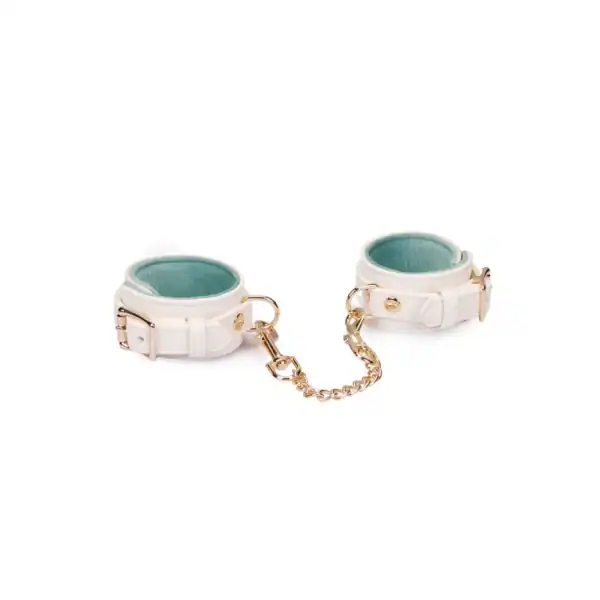 Boudoir Amor handcuffs by Liebe Seele, in light-colored leather with gold chain and snap hooks, presented flat on a light-colored background in the Brigade Mondaine Paris universe.