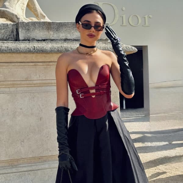 Daelos leather corset RE:STRICT Brigade Mondaine Paris Model wearing Daelos corset in red RE:STRICT leather at Brigade Mondaine Paris, structured plunging neckline, adjustable straps, worn with matching accessories on red background.