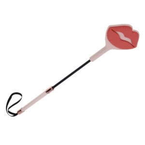 Látigo BDSM con diseño decorativo de labios, mango delgado y correa para la muñeca, presentado por Brigade Mondaine Paris sobre fondo claro.