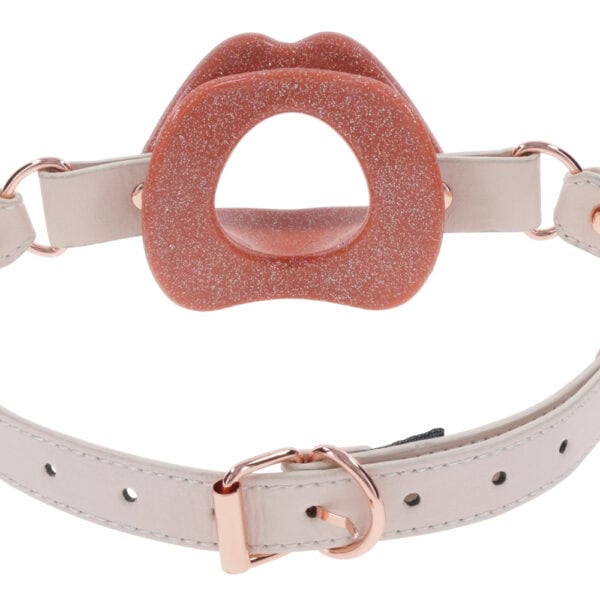 Open gag in lip design with clear strap and metal finishes, presented by Brigade Mondaine Paris on clear background.