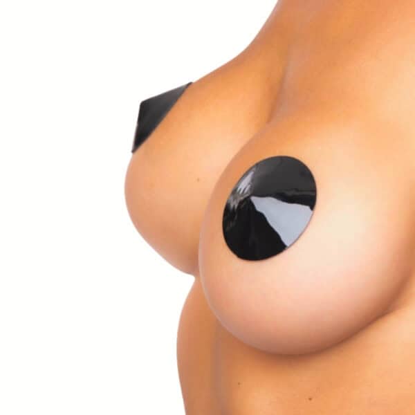 Close-up of a breast wearing round black nipple covers with a varnish finish and a smooth, shiny surface, worn directly on the skin.