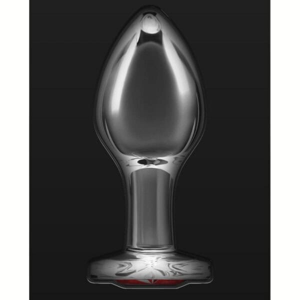 Plug anal en cristal transparent posé sur fond noir, avec une base décorative en forme de cœur rouge facetté, à l’esthétique élégante et raffinée.