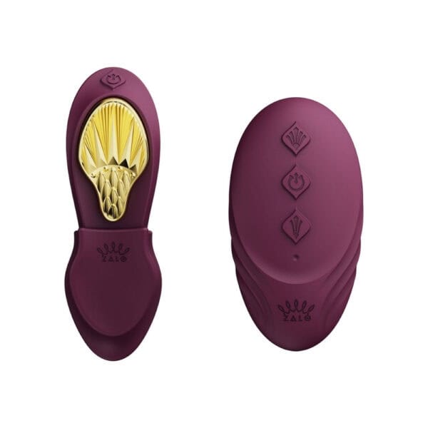 Plum-colored portable vibrator with gold details, ergonomic design and integrated controls, presented on a white background, selection Brigade Mondaine Paris.