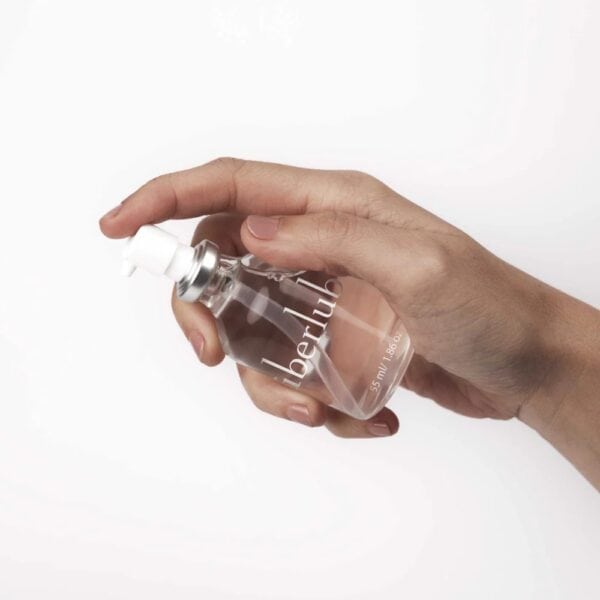 Lubrifiant Luxe Überlube Flacon en verre de lubrifiant luxe transparent avec spray, présenté avec son étui cylindrique blanc, sélection Brigade Mondaine Paris.