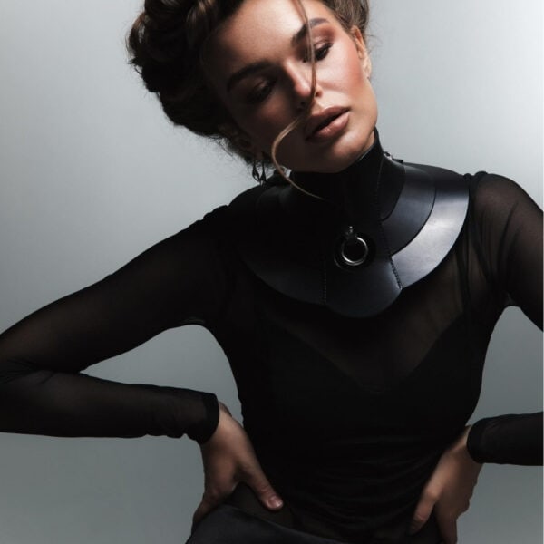 Halsband Posture Hold RE:STRICT Brigade Mondaine Paris Model trägt die RE:STRICT Posture Hold Halskette aus schwarzem Leder bei Brigade Mondaine Paris, ein steifes Stück, das den Hals bedeckt, zentraler Metallring, getragen mit einem schwarzen Mesh-Top im Studio.