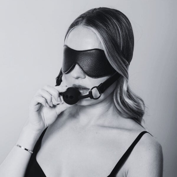Stirnband aus schwarzem Leder mit elastischem Riemen und integriertem schwarzem Silikon-Gag, BDSM-Zubehör, angeboten von Brigade Mondaine Paris.