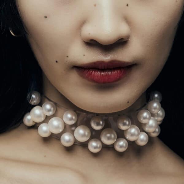 Modell trägt Boudoir Choker Perlensau mit weißen Perlen, die auf einer transparenten Basis montiert sind, angeboten von Brigade Mondaine Paris.