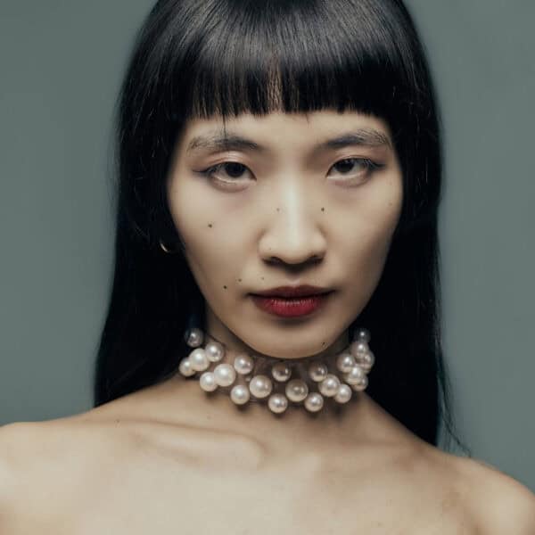 Modell trägt Boudoir Choker Perlensau mit weißen Perlen, die auf einer transparenten Basis montiert sind, angeboten von Brigade Mondaine Paris.