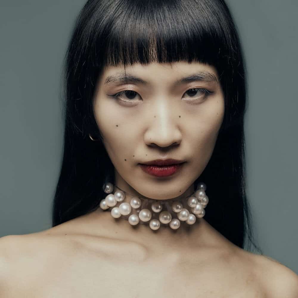 Modell trägt Boudoir Choker Perlensau mit weißen Perlen, die auf einer transparenten Basis montiert sind, angeboten von Brigade Mondaine Paris.