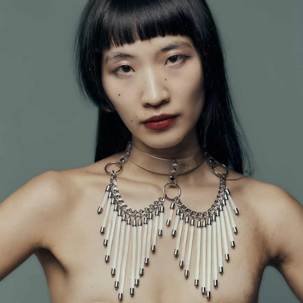 Modell trägt den Cosmic Choker Perlensau aus transparentem Material mit Metallketten und hängenden Troddeln, angeboten von Brigade Mondaine Paris.