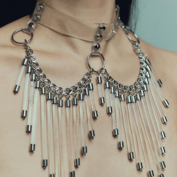 Modelo que lleva el Cosmic Choker Perlensau en material transparente con cadenas de metal y colgantes, ofrecido por Brigade Mondaine Paris.