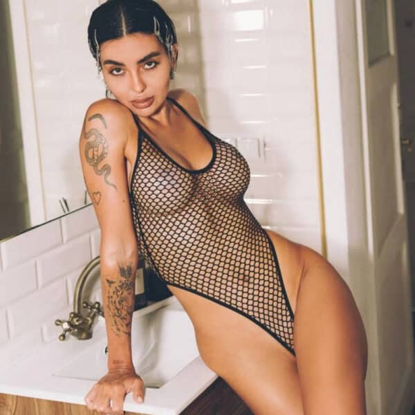 Black bodysuit in fine Pivovarova fishnet, scalloped cut and thin straps, worn on a feminine silhouette in an interior, selection Brigade Mondaine Paris.