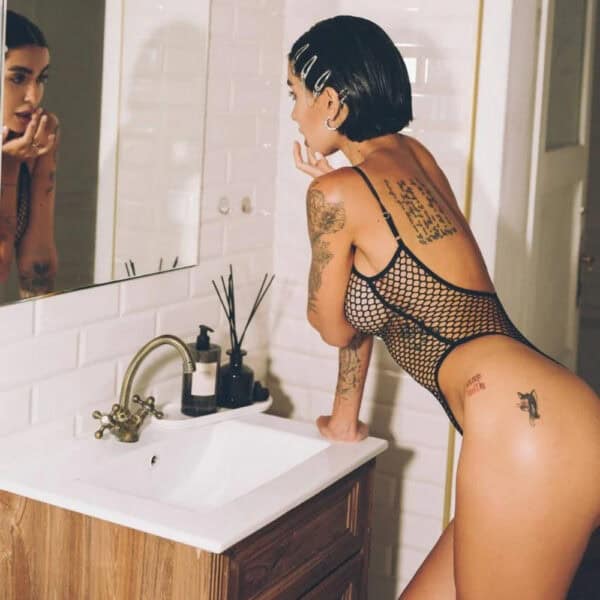 Black bodysuit in fine Pivovarova fishnet, scalloped cut and thin straps, worn on a feminine silhouette in an interior, selection Brigade Mondaine Paris.