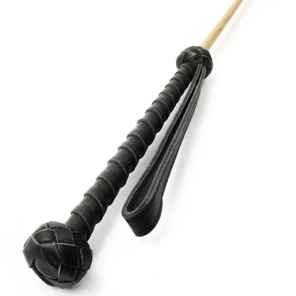 Bastón Obediance de madera clara con empuñadura de cuero negro y correa de mano a juego, accesorio ofrecido por Brigade Mondaine Paris.